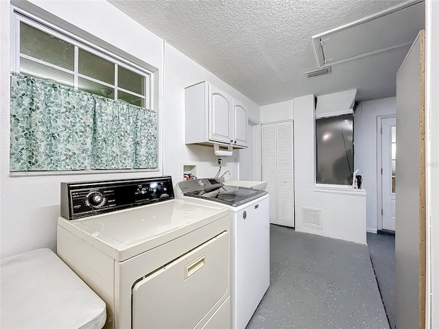 washroom with washer and dryer, a textured ceiling, and cabinets