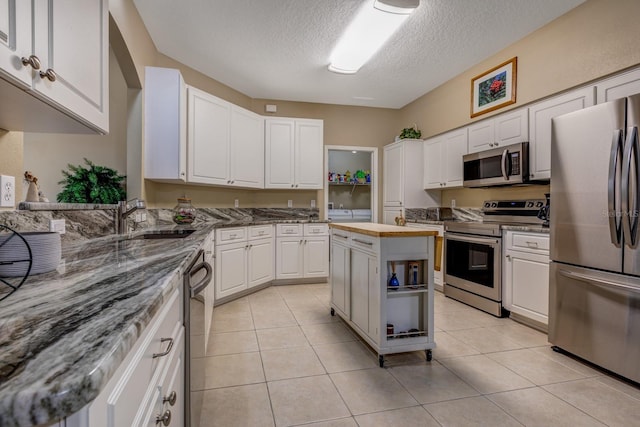 kitchen featuring appliances with stainless steel finishes, sink, a textured ceiling, white cabinets, and dark stone countertops