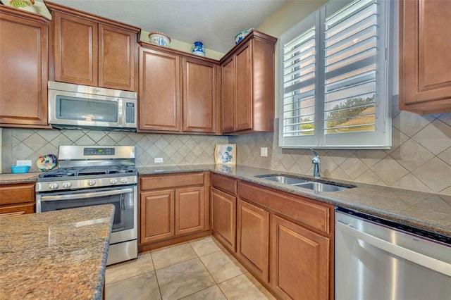 kitchen with backsplash, appliances with stainless steel finishes, light tile patterned floors, stone counters, and sink