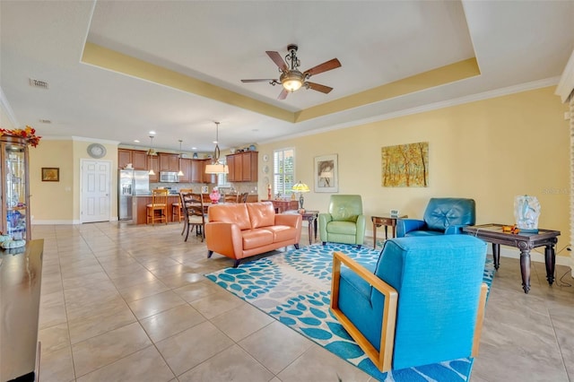 living room featuring ceiling fan, a raised ceiling, ornamental molding, and light tile patterned floors