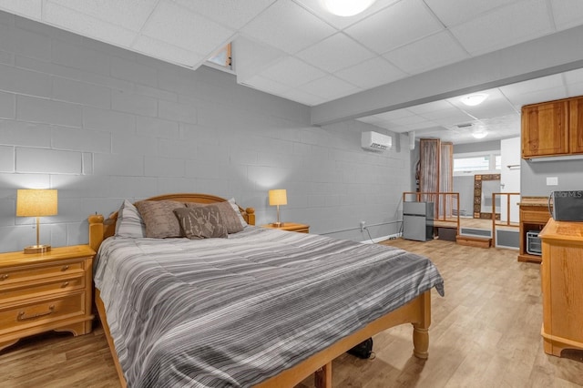 bedroom with a wall unit AC, light hardwood / wood-style floors, and a paneled ceiling