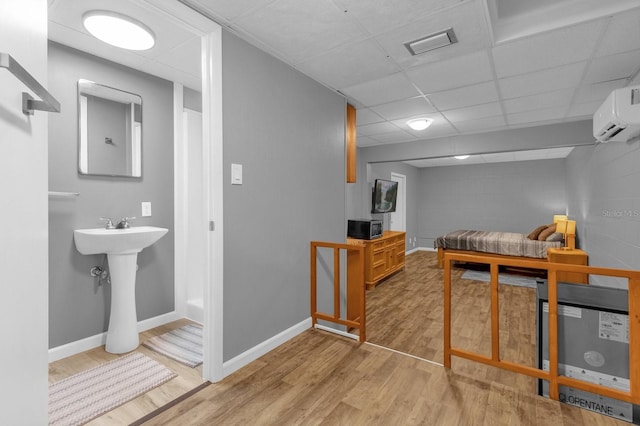 bedroom with a paneled ceiling, a wall unit AC, sink, and light hardwood / wood-style floors