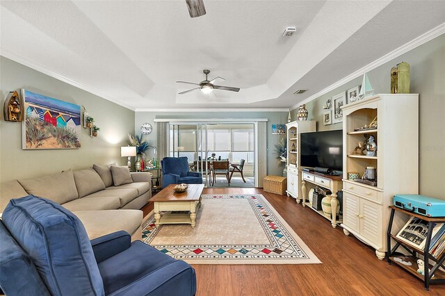 living room featuring dark wood-type flooring, ceiling fan, ornamental molding, and a tray ceiling