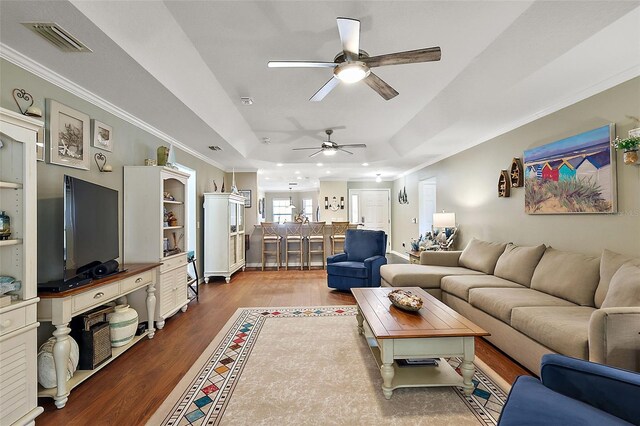 living room featuring ceiling fan, ornamental molding, a tray ceiling, and hardwood / wood-style floors