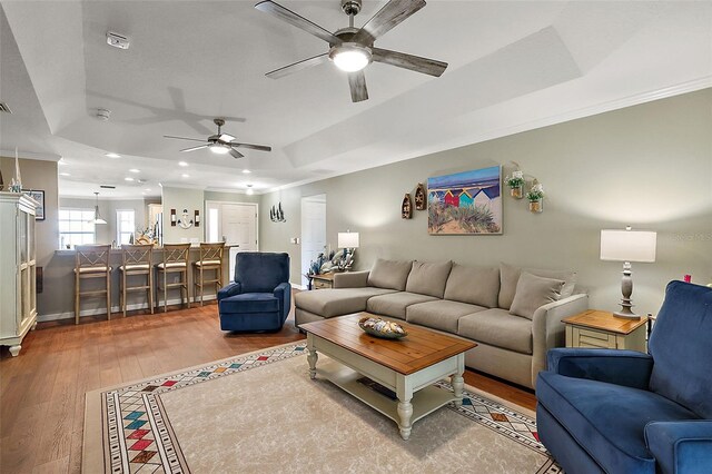 living room with ornamental molding, light hardwood / wood-style flooring, a tray ceiling, and ceiling fan