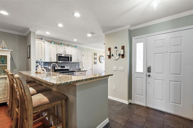 kitchen with decorative backsplash, appliances with stainless steel finishes, a kitchen breakfast bar, light stone countertops, and crown molding