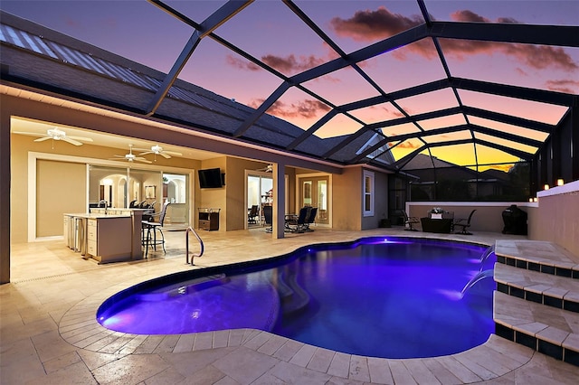 pool at dusk featuring a patio, glass enclosure, pool water feature, and ceiling fan