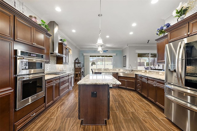 kitchen with a kitchen island, wall chimney range hood, kitchen peninsula, stainless steel appliances, and decorative light fixtures