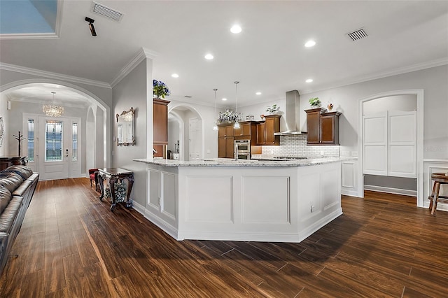 kitchen with wall chimney range hood, stainless steel oven, hanging light fixtures, dark wood-type flooring, and ornamental molding