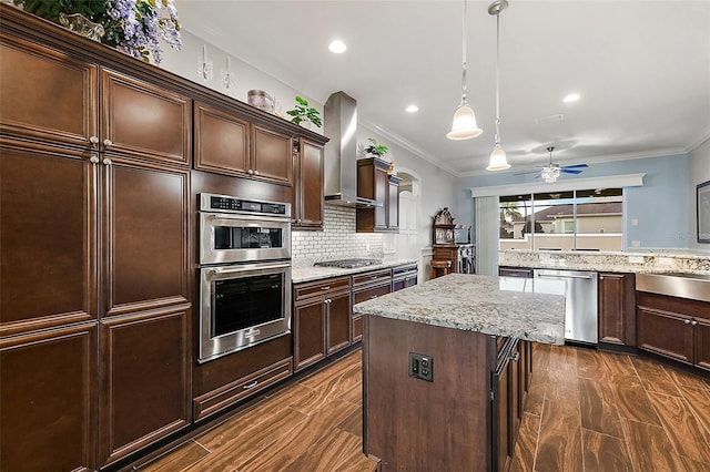 kitchen with dark hardwood / wood-style floors, wall chimney exhaust hood, hanging light fixtures, a center island, and appliances with stainless steel finishes