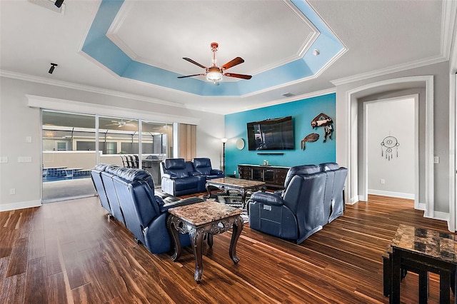 living room featuring ornamental molding, a tray ceiling, dark wood-type flooring, and ceiling fan