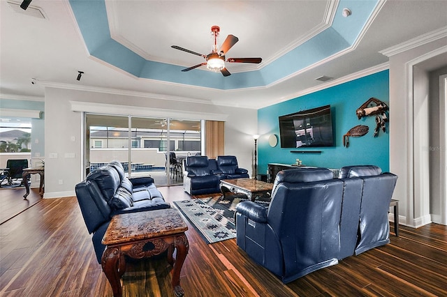 living room featuring ornamental molding, dark wood-type flooring, a tray ceiling, and ceiling fan