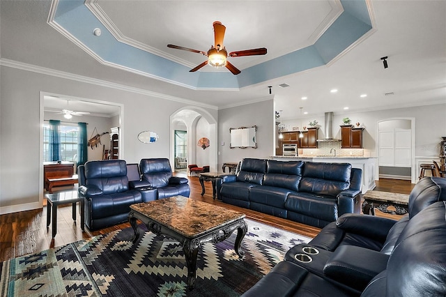 living room with dark wood-type flooring, ceiling fan, a raised ceiling, and ornamental molding