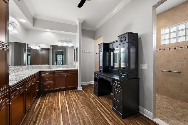 bathroom featuring wood-type flooring, ceiling fan, tiled shower, vanity, and ornamental molding