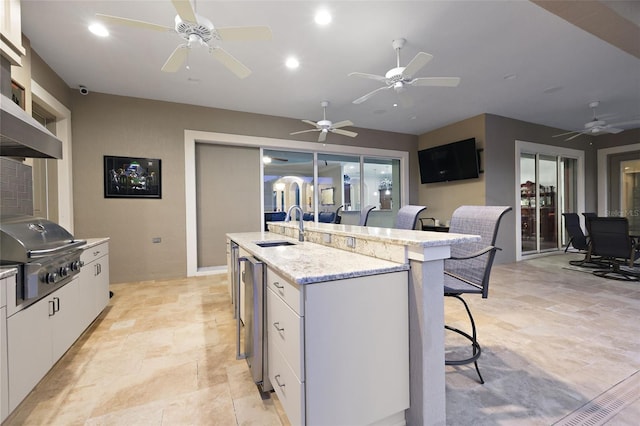 kitchen with light stone counters, a kitchen breakfast bar, white cabinetry, a kitchen island with sink, and sink