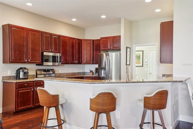 kitchen with a kitchen bar, kitchen peninsula, stainless steel appliances, and dark hardwood / wood-style floors