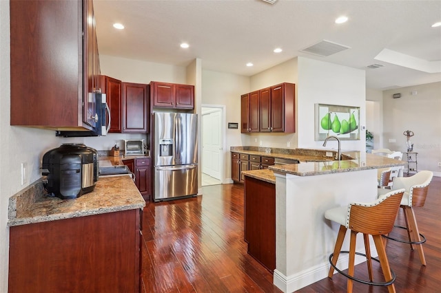 kitchen featuring sink, stainless steel appliances, light stone counters, a breakfast bar area, and dark hardwood / wood-style floors