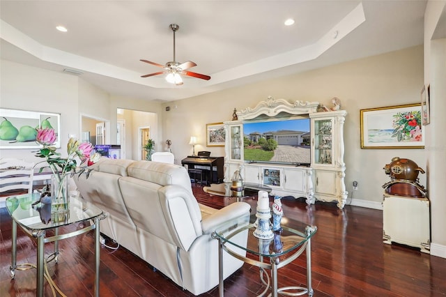 living room featuring ceiling fan, a tray ceiling, and dark hardwood / wood-style flooring