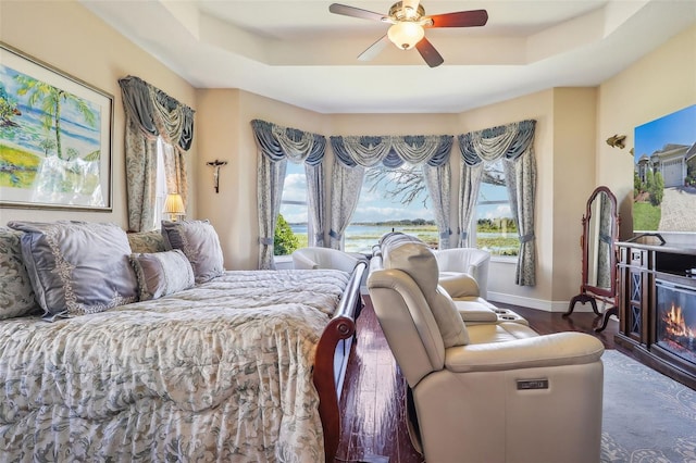 bedroom with dark hardwood / wood-style floors, a tray ceiling, and ceiling fan