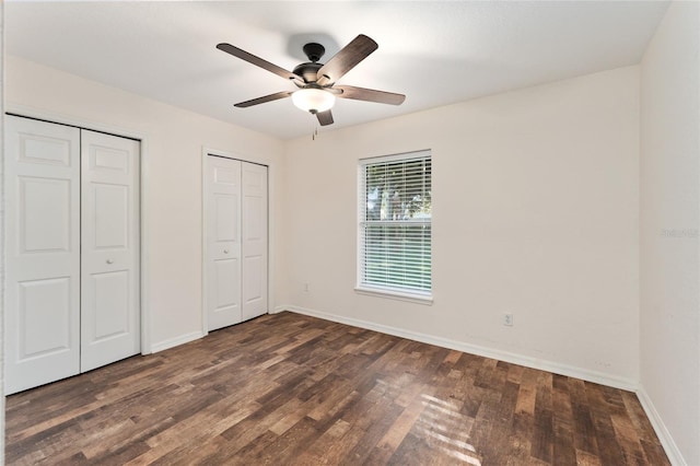 unfurnished bedroom with ceiling fan, dark hardwood / wood-style flooring, and multiple closets