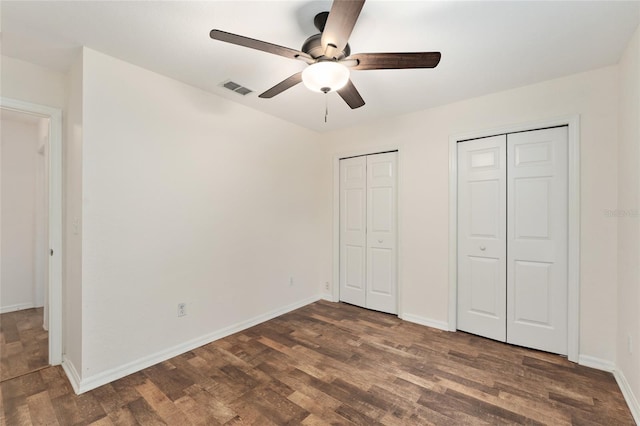 unfurnished bedroom with ceiling fan, dark hardwood / wood-style floors, and two closets