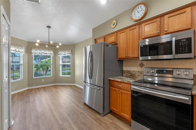 kitchen featuring backsplash, a textured ceiling, light wood-type flooring, a notable chandelier, and stainless steel appliances