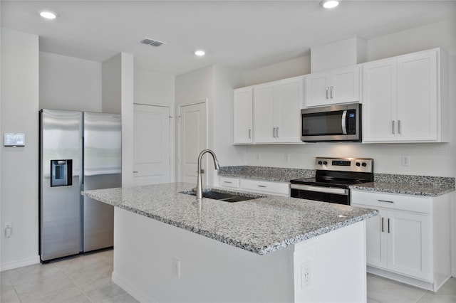 kitchen featuring light stone counters, visible vents, a sink, a center island with sink, and appliances with stainless steel finishes