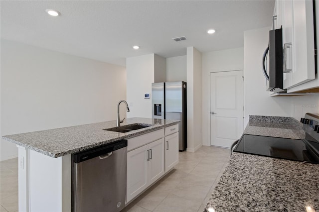 kitchen with white cabinets, light stone counters, stainless steel appliances, a sink, and a kitchen island with sink