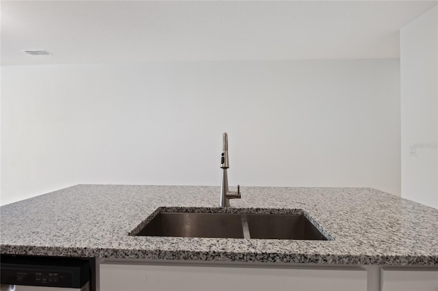 interior details with dishwasher, visible vents, light stone counters, and a sink
