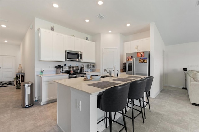 kitchen featuring light tile patterned floors, a kitchen bar, a center island with sink, white cabinets, and appliances with stainless steel finishes