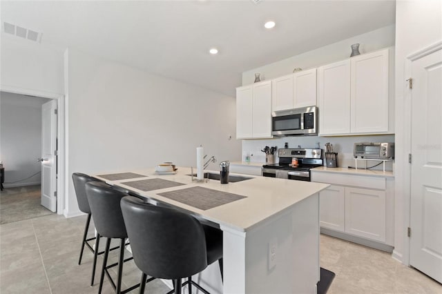 kitchen featuring a kitchen island with sink, sink, appliances with stainless steel finishes, white cabinetry, and a breakfast bar area