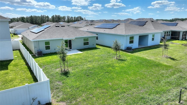 back of property with central air condition unit, a yard, and solar panels