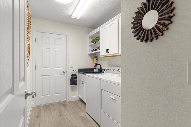 washroom featuring sink, separate washer and dryer, a textured ceiling, cabinets, and light hardwood / wood-style flooring