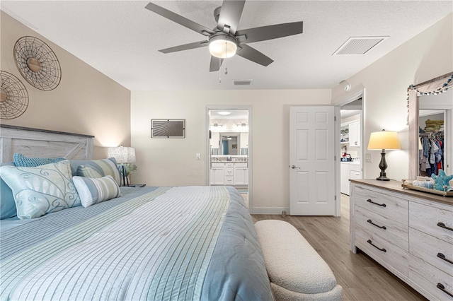 bedroom featuring ceiling fan, a textured ceiling, connected bathroom, light hardwood / wood-style flooring, and a closet