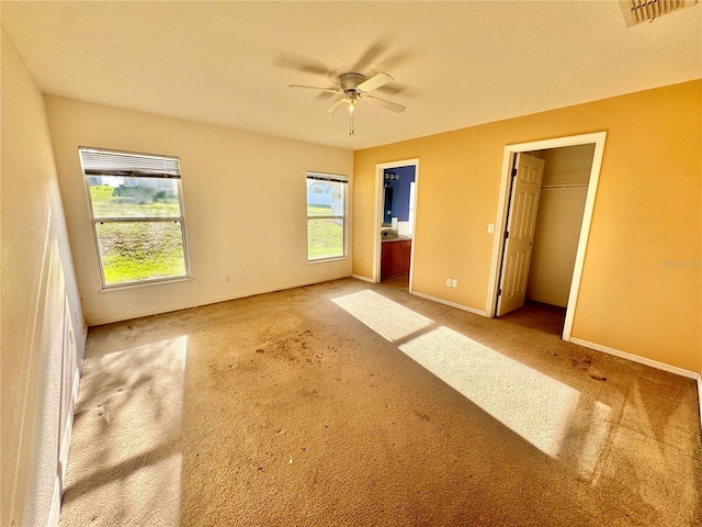 unfurnished bedroom with ensuite bathroom, ceiling fan, multiple windows, and a walk in closet