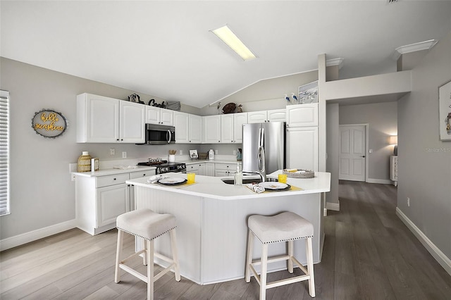 kitchen featuring white cabinets, a kitchen bar, stainless steel appliances, and a center island with sink