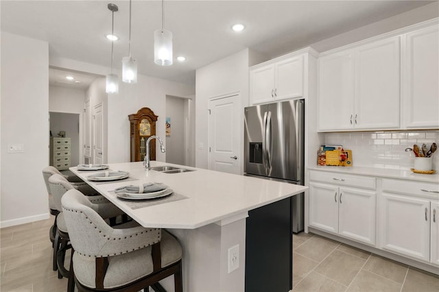 kitchen featuring decorative backsplash, a kitchen island with sink, stainless steel fridge, decorative light fixtures, and white cabinetry