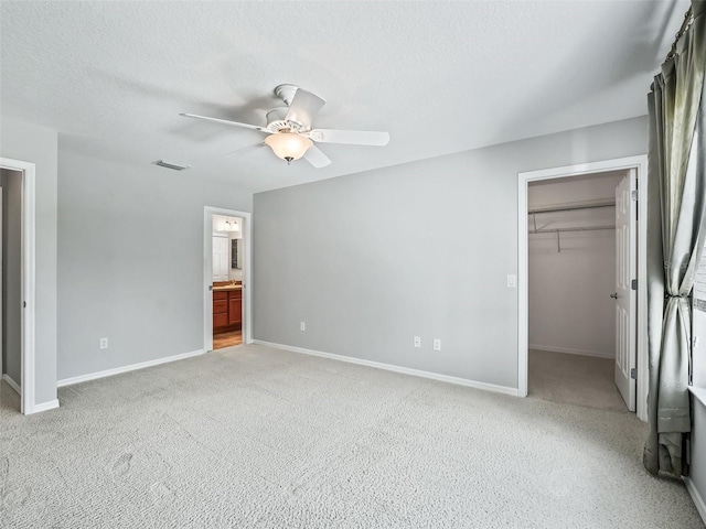 unfurnished bedroom with a spacious closet, ensuite bath, a closet, ceiling fan, and light carpet