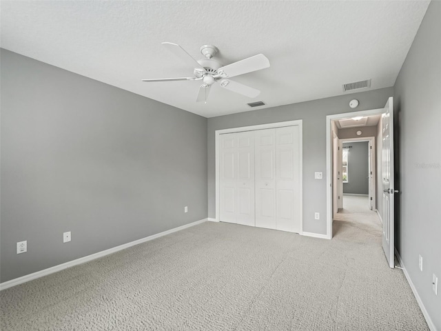 unfurnished bedroom with light carpet, a textured ceiling, a closet, and ceiling fan