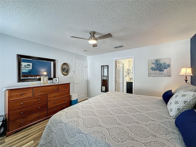 bedroom featuring ensuite bathroom, a textured ceiling, light wood-type flooring, and ceiling fan