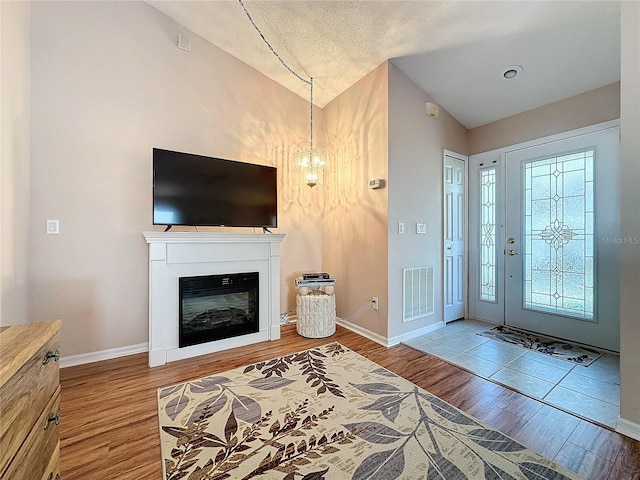 foyer entrance featuring lofted ceiling, hardwood / wood-style floors, a textured ceiling, and an inviting chandelier