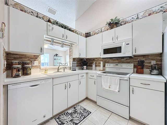 kitchen featuring white appliances, sink, a textured ceiling, white cabinetry, and vaulted ceiling