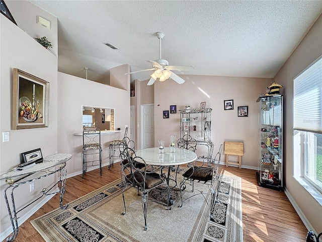 dining space with lofted ceiling, a textured ceiling, wood-type flooring, and ceiling fan