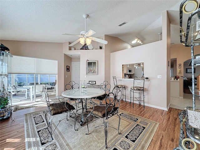 dining room featuring a textured ceiling, wood-type flooring, high vaulted ceiling, and ceiling fan