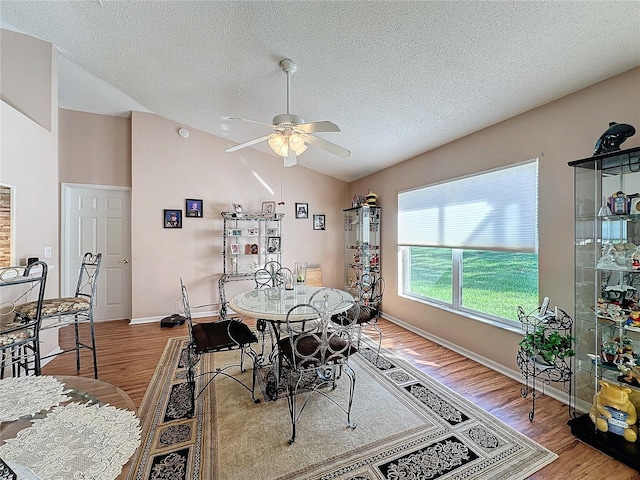 dining area with ceiling fan, a textured ceiling, wood-type flooring, and vaulted ceiling