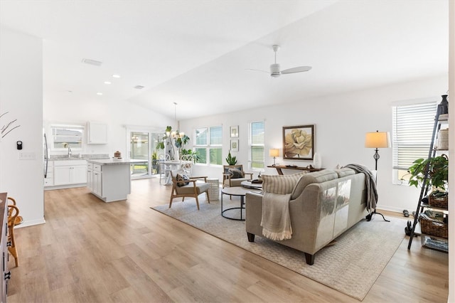 living room featuring lofted ceiling, light hardwood / wood-style flooring, and ceiling fan with notable chandelier