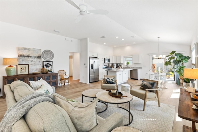 living room with lofted ceiling, a wealth of natural light, light wood-type flooring, and ceiling fan with notable chandelier