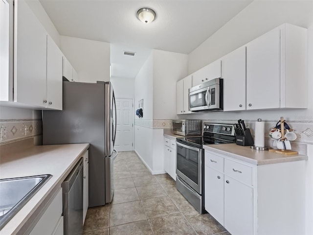 kitchen featuring sink, stainless steel appliances, light tile patterned floors, and white cabinets