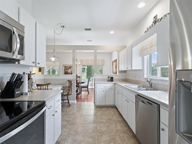 kitchen with a healthy amount of sunlight, appliances with stainless steel finishes, decorative light fixtures, and white cabinets