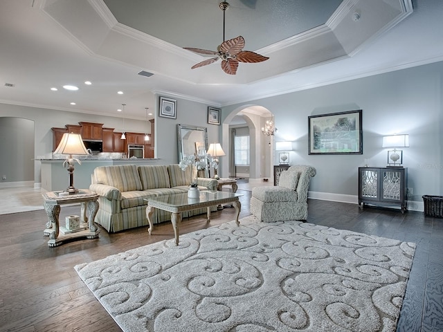 living room featuring ornamental molding, ceiling fan, a tray ceiling, and dark hardwood / wood-style flooring